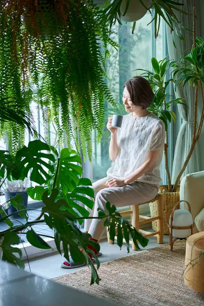 Etrafı saksılarla çevrili orta yaşlı bir kadın dinleniyor.