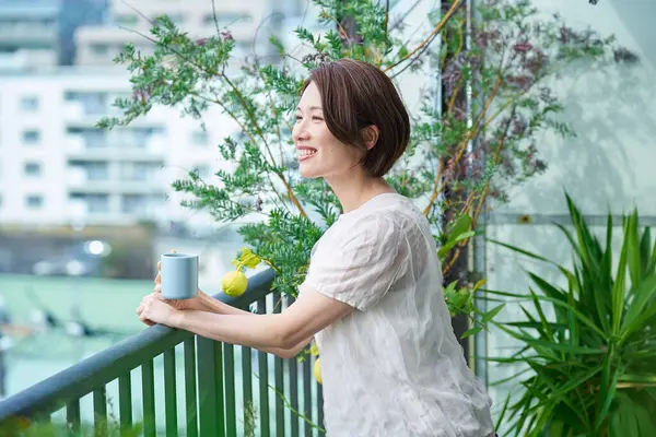 Balkonda bir kupa tutan rahat bir yüzü olan bir kadın.