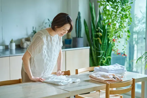 Orta yaşlı bir kadın oturma odasında çamaşır katlıyor.