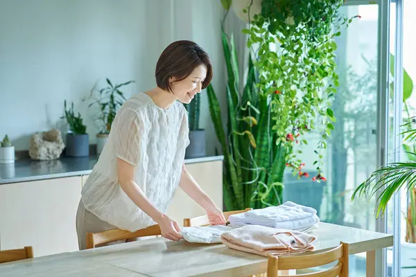 Orta yaşlı bir kadın oturma odasında çamaşır katlıyor.