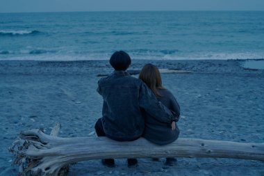 Gün batımından hemen sonra sahilde yürüyen genç bir adam ve kadın.