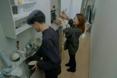 Genç adam ve kadın odada birlikte yemek pişiriyorlar.