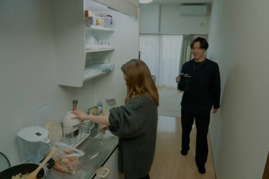Genç adam ve kadın odada birlikte yemek pişiriyorlar.