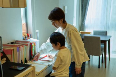 Evindeki odasında ders çalışan bir çocuk, annesi tarafından izleniyor.