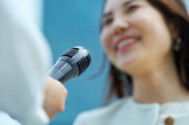 Açık havada röportaj yapan gülümseyen genç bir kadın.