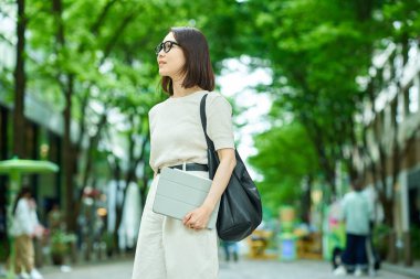 Yeşil bir sokakta yürüyen genç bir kadın