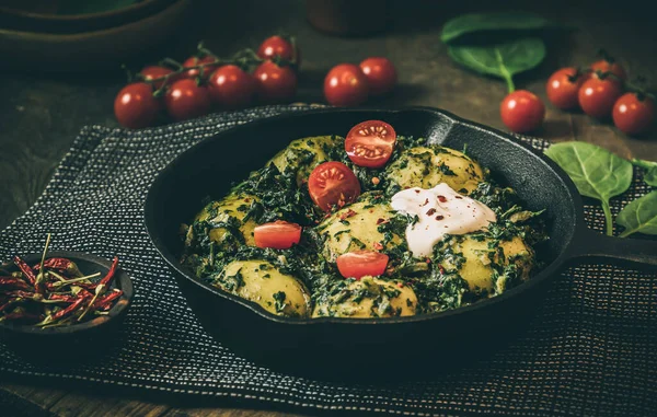 Potato pan with spinach, vegetarian cuisine, on dark rustic table