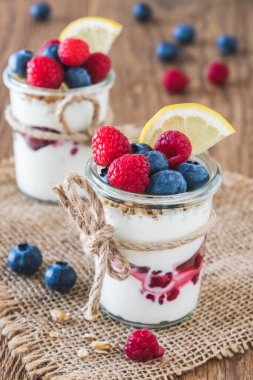 Çilekli yoğurt ve mısır gevreği kırsal bir tahta masada, dikey bir bardakta.