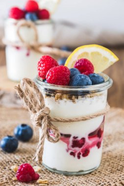 Çilekli yoğurt ve mısır gevreği kırsal bir tahta masada, dikey bir bardakta.