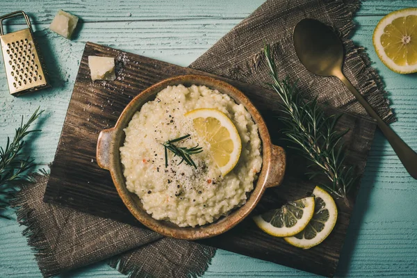 Lemon rice risotto with rosemary and fresh lemon slices on light green background, top view