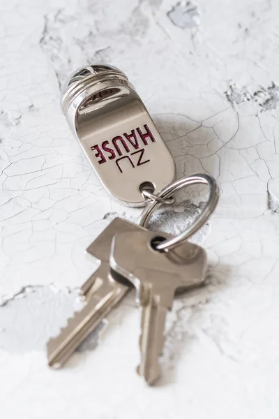Key ring with two keys and tag with German text Zu Hause (translation: at home) on a white background, vertical with copy space