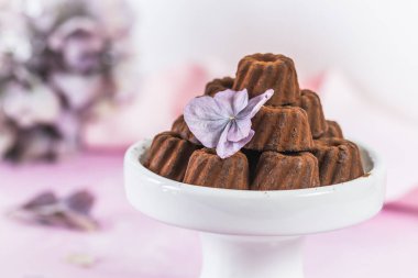 Çikolatalı pralinler, kakao tozlu, açık pembe arka planda, ortanca çiçeğiyle süslenmiş küçük Bundt kekleri şeklinde.
