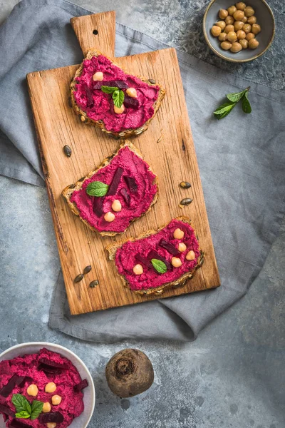 stock image Wooden board of bread slices with beetroot hummus on a gray background, top view