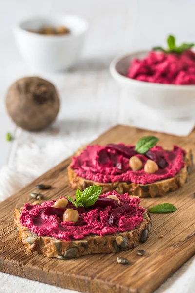 stock image Wooden board of bread slices with beetroot hummus on a white wooden background, vertical