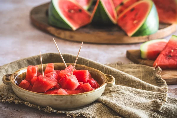 Pieces of watermelon as finger food on a plate, sliced watermelon in the background
