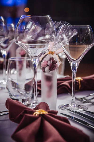 Wine glasses and candy in a shot glass as a decoration on a festive table setting in dark red colors, vertical