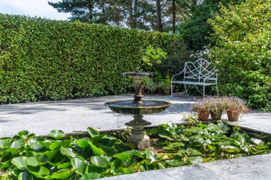 Havuzu, antika çeşmesi ve metal bahçe tezgahı olan güzel bir flagstone bahçesi.