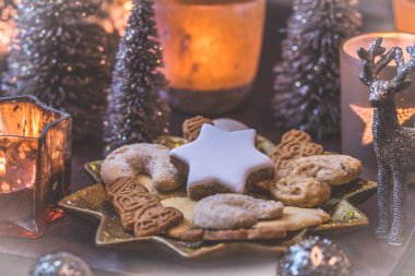 Yılbaşı süsleri ve mum ışıkları olan yıldız şeklinde bir tabakta Noel kurabiyeleri.