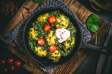 Potato pan with spinach, vegetarian cuisine, on dark rustic table