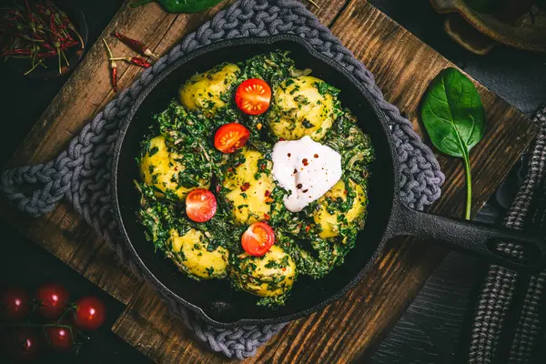 Potato pan with spinach, vegetarian cuisine, on dark rustic table