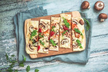 Taze pişmiş flamkuchen, geleneksel Fransız tarte flambee ya da vejetaryen bir tarifte mantar, krem peynir, domates ve roka, açık yeşil ahşap tahta ve masa üzerinde Alman pizzası. Üst görünüm.