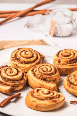 Beyaz mermer zemin üzerinde beyaz tabakta ev yapımı tarçın ruloları, dikey