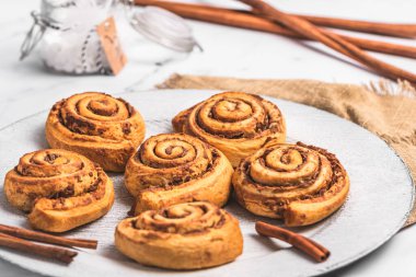 Beyaz mermer zemin üzerinde beyaz tabakta ev yapımı tarçın ruloları