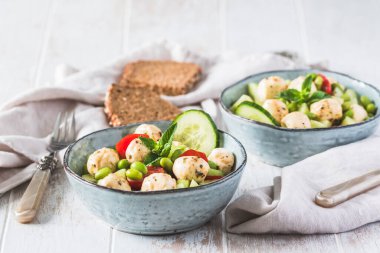 Salatalıklı yaz salatası, mini domatesler, mini mozzarella ve soya fasulyesi beyaz ahşap arka planda, kopyalama alanı