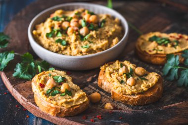 Humus, kase içinde nohut püresi ve mavi ahşap arka planda kızarmış ekmek dilimleri.