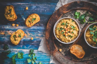 Humus, nohut püresi kasede ve kızarmış ekmek dilimleri mavi ahşap arka planda, üst manzara