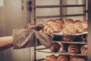 Fırınlanmış kruvasan tepsisini tramvaya iten fırın eldivenli bir adam.