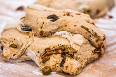 Zeytinli, domatesli ve otlu çiğ ekmek hamuru, ahşap çalışma masasında, bir fırında daha fazla işlem için hazırlanır..