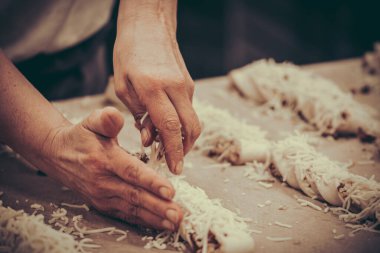 Bir fırıncı fırındaki fırın tepsisine çiğ hamur ekmeğine peynir koyar. Buğdaylı vintage tarzı.