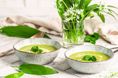 Açık gri arka planda iki kase yabani sarımsak çorbası, bitki çorbası.