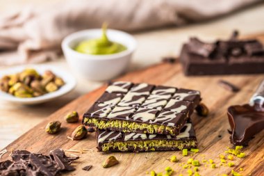 Beyaz ve koyu çikolatalı ev yapımı Dubai çikolatası, fıstıklı krema, kadayif ve ahşap arka planda şam fıstığı.