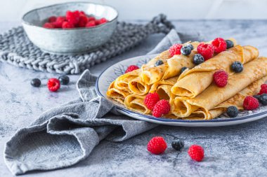 Açık mavi zemin üzerinde ahududu ve yaban mersinli rulo krep yığını.