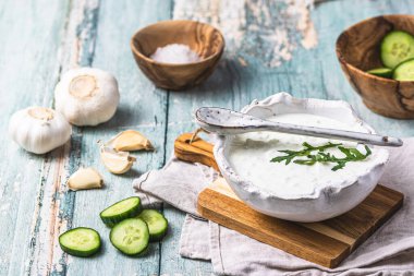 Yunan tzatziki, ahşap arka planda salatalık ve sarımsak bulunan el yapımı beyaz bir toprak kapta.