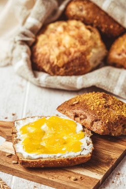 Krem peynirli ve limonlu yarım rulo, arka planda çeşitli ekmek ruloları, kahvaltı sahnesi, dikey