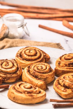 Beyaz mermer zemin üzerinde beyaz tabakta ev yapımı tarçın ruloları, dikey