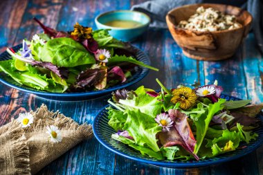 Karışık çeşitleri olan taze salata ve kırsal mavi ahşap arka planda yenilebilir çiçekler.