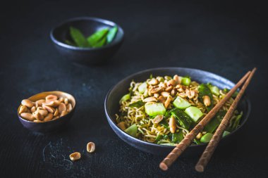 Taze soğan ve bezelyeli Asya usulü erişte. Üstünde salatalık ve kavrulmuş fıstık var.