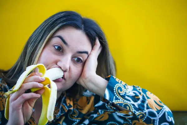 laughing woman eating banana, yellow background