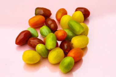 Farklı renklerde kokteyl domatesleri, kırmızı, turuncu, yeşil, pastel arka planda sarı.