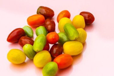 Farklı renklerde kokteyl domatesleri, kırmızı, turuncu, yeşil, pastel arka planda sarı.