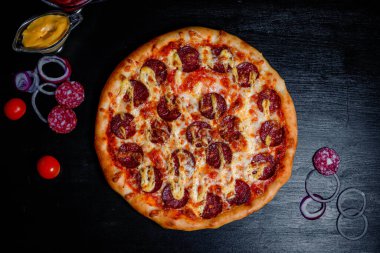 Tasty pepperoni pizza and cooking ingredients tomatoes  on black concrete background. Top view of hot pepperoni pizza.With copy space for text