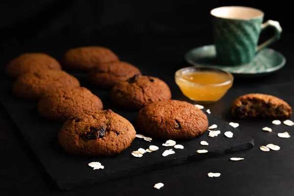 暗いテーブルの上にオートミールクッキー 蜂蜜と紅茶のカップのぼやけたイメージ お茶を飲むという概念 — ストック写真