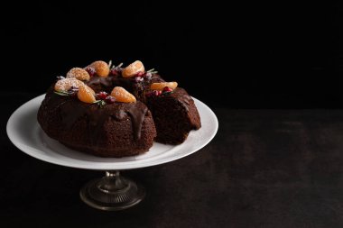 On a black background with a place for writing text on a stand, a chocolate cake is decorated with fruits. The concept of writing a recipe.