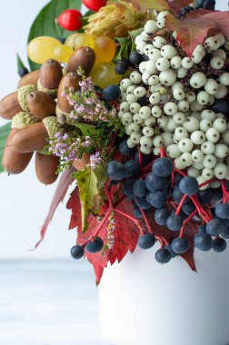 Blurred image of a bouquet with autumn bright leaves, berries, acorns on a light background. Natural background.