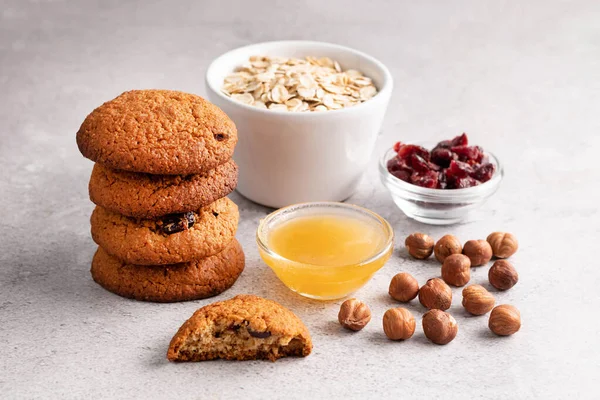 Blurred image of oatmeal cookies, honey in a plate, nuts, dried cranberries and oatmeal in the background.The concept of a recipe for making oatmeal cookies.