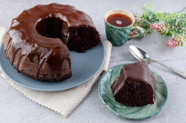 Çikolatalı kek ve tabakta bir dilim, bir fincan kahve ve gri masada bir kaşık.